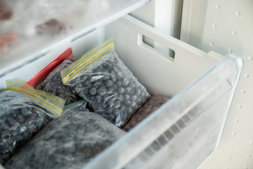 An open freezer drawer packed with sealed bags of frozen berries, frosted over