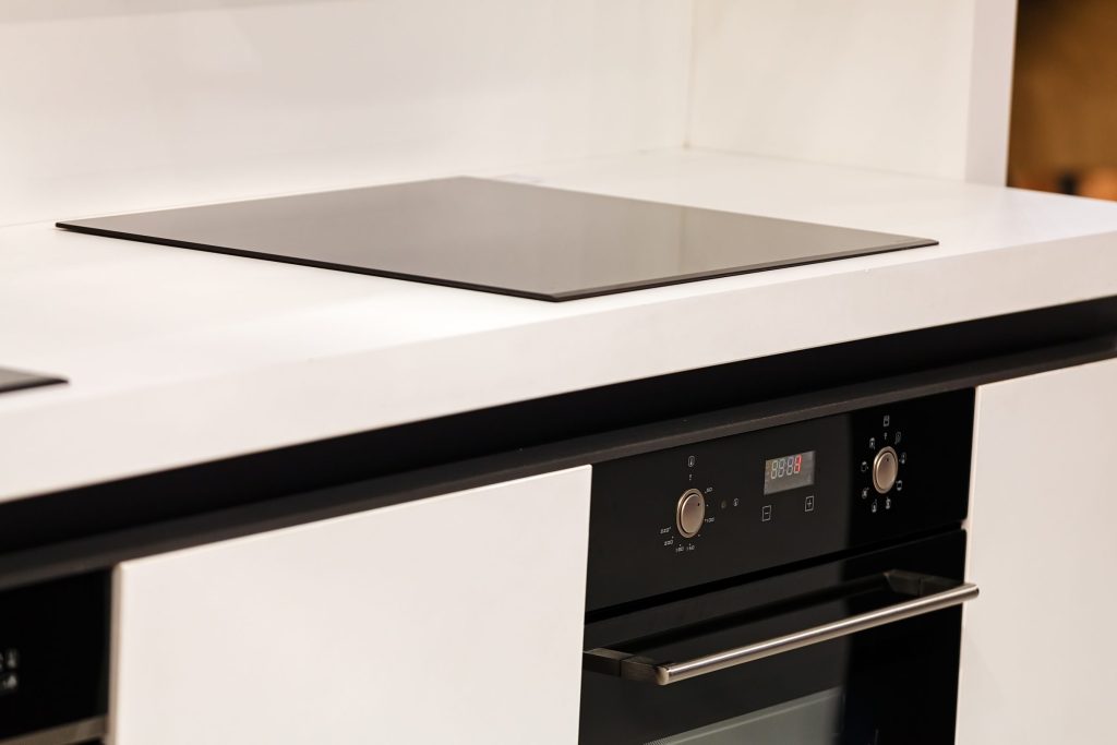 A black glass cooktop set flush into a white kitchen counter with a built-in oven below it