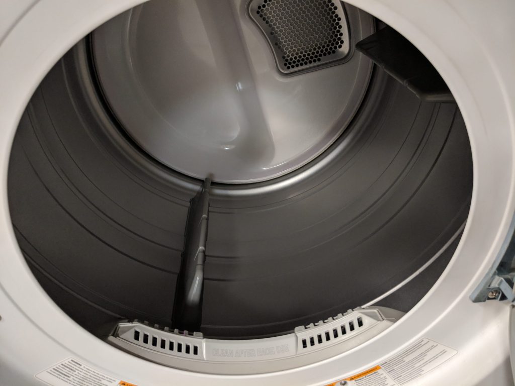 The inside of a white clothes dryer drum, lint filter and vent grille visible at the door