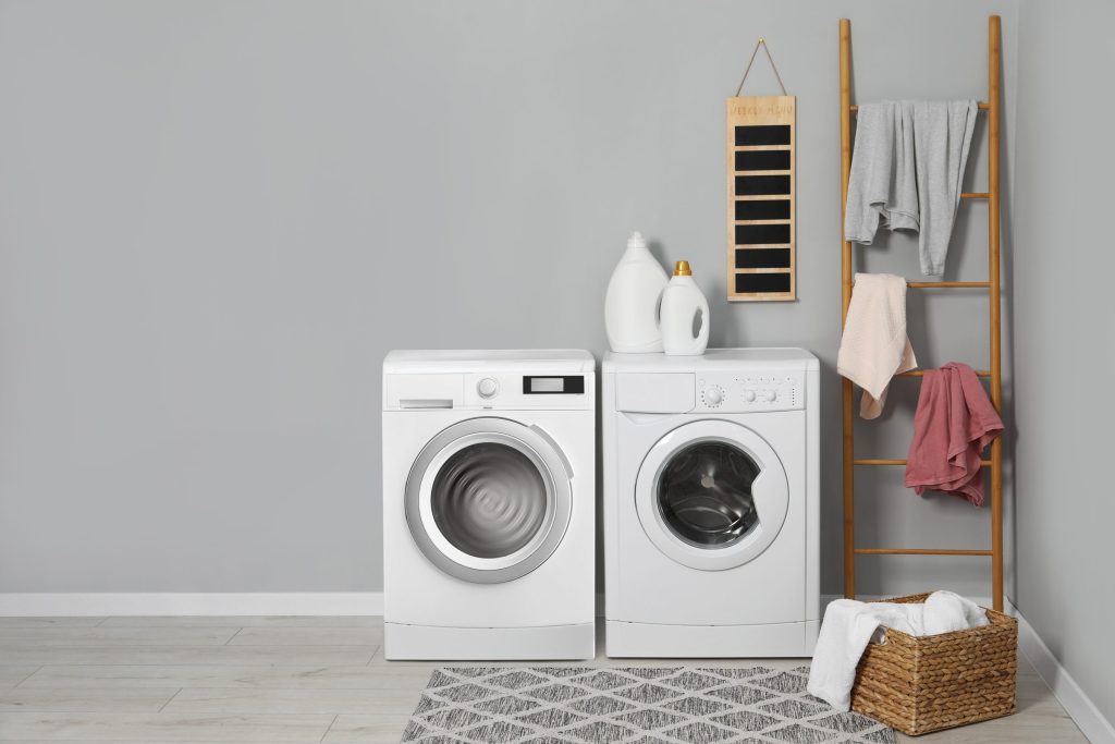 A washing machine and a dryer side by side in a bright laundry room, a wooden ladder with towels beside them