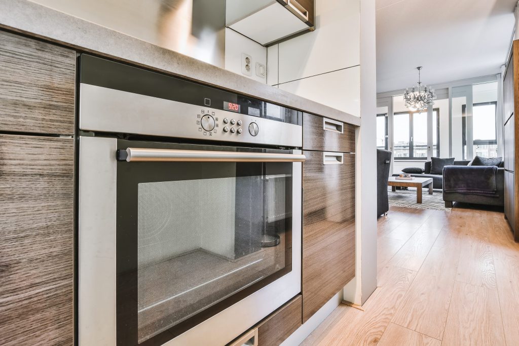 A built-in wall oven set into wood cabinetry in a modern kitchen, its control panel lit