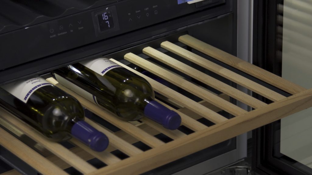 A wooden wine shelf pulled out of a chilled wine drawer, bottles lying on it, the temperature display lit above