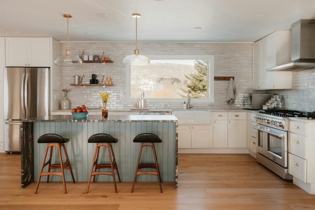 A bright kitchen with a green island, three stools and a range under a hood