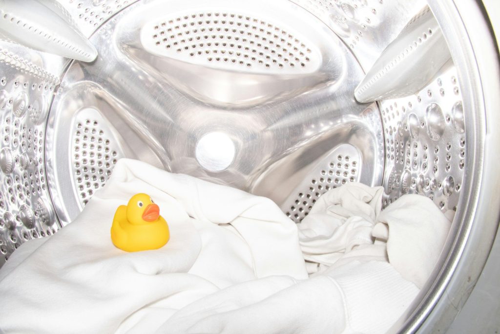 A rubber duck sitting on white washing inside a stainless drum