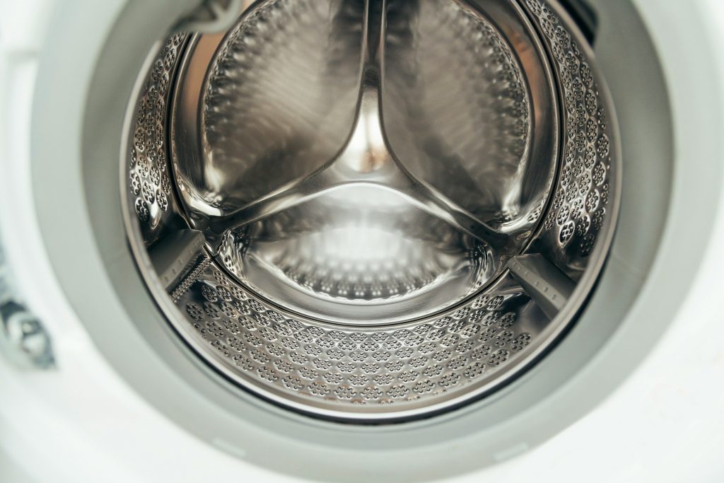 The inside of an empty stainless washing drum, lit from the door