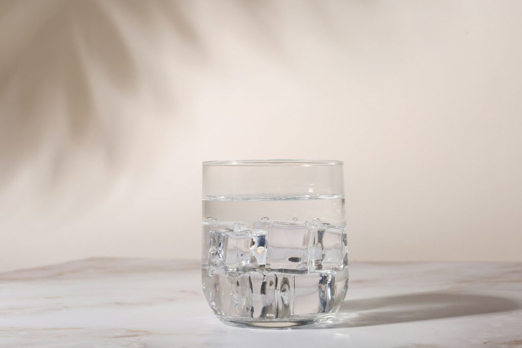 A glass of iced water on a marble counter in leaf shadow