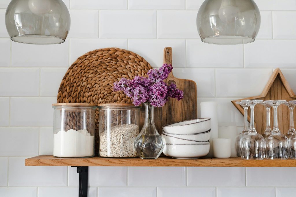 An open timber shelf of jars, bowls and glasses against white tile