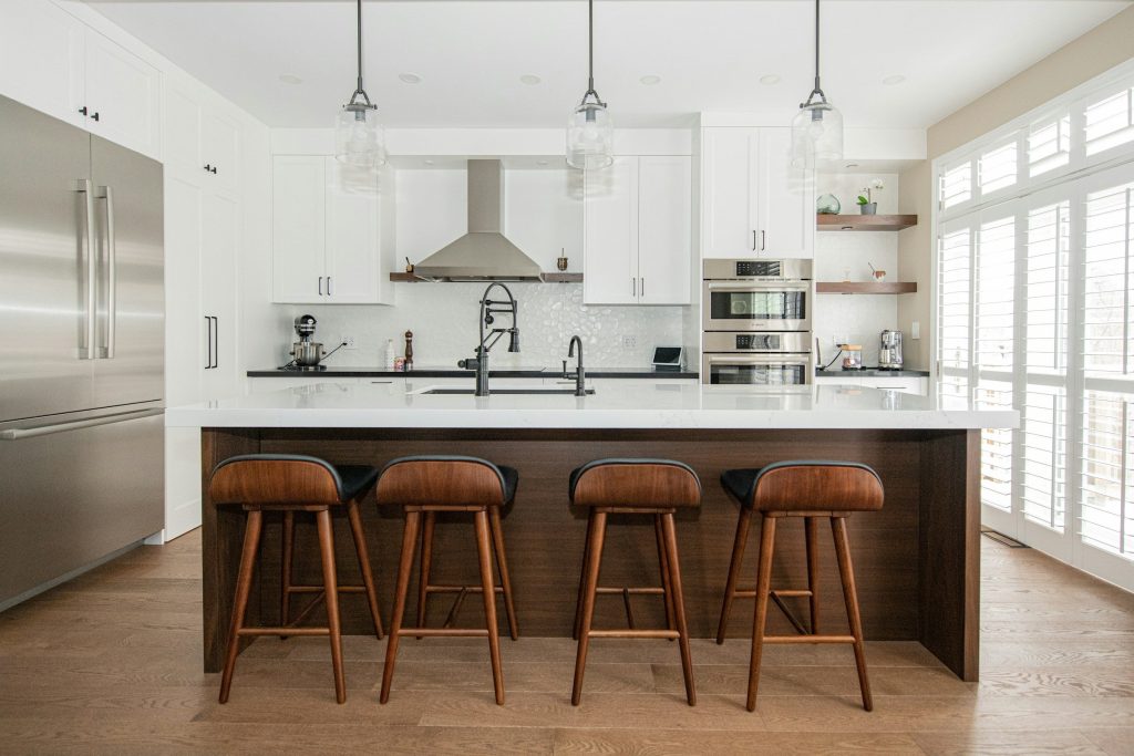 A counter-depth French-door refrigerator in stainless steel, set flush with white cabinetry beside a kitchen island