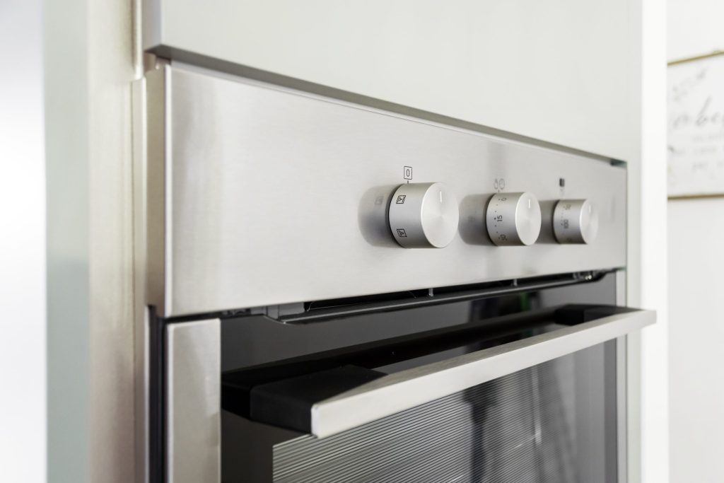 A stainless built-in wall oven with its door slightly open and three control knobs on the fascia