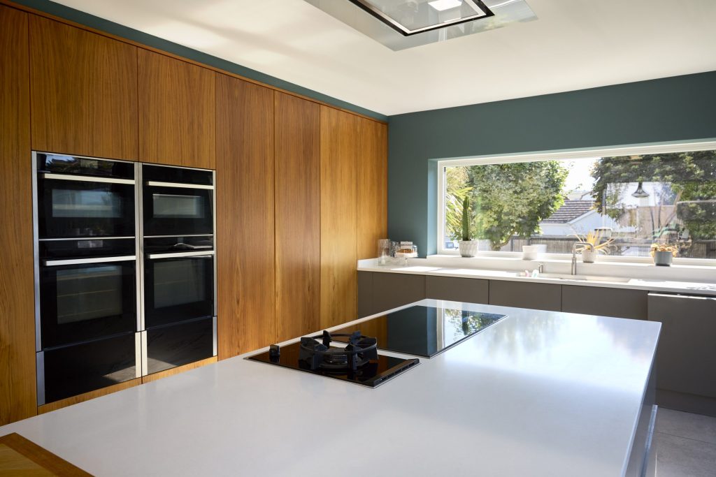 Two stacked built-in ovens set into a walnut cabinet run, with an induction hob on the island in front