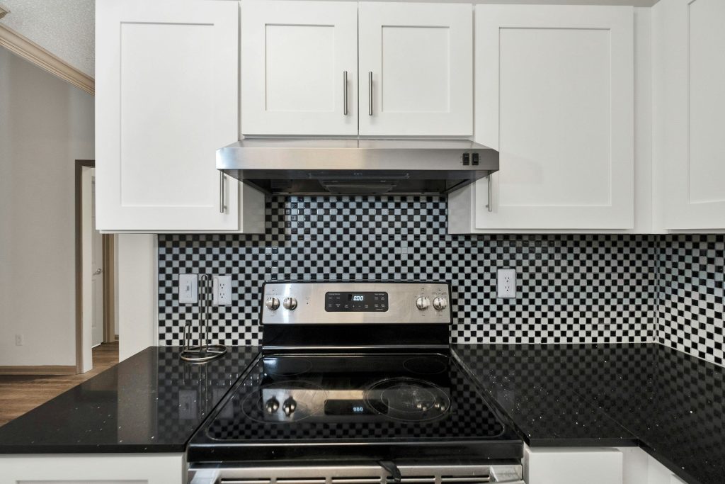 A stainless under-cabinet range hood fitted beneath white wall cabinets above a mosaic splashback