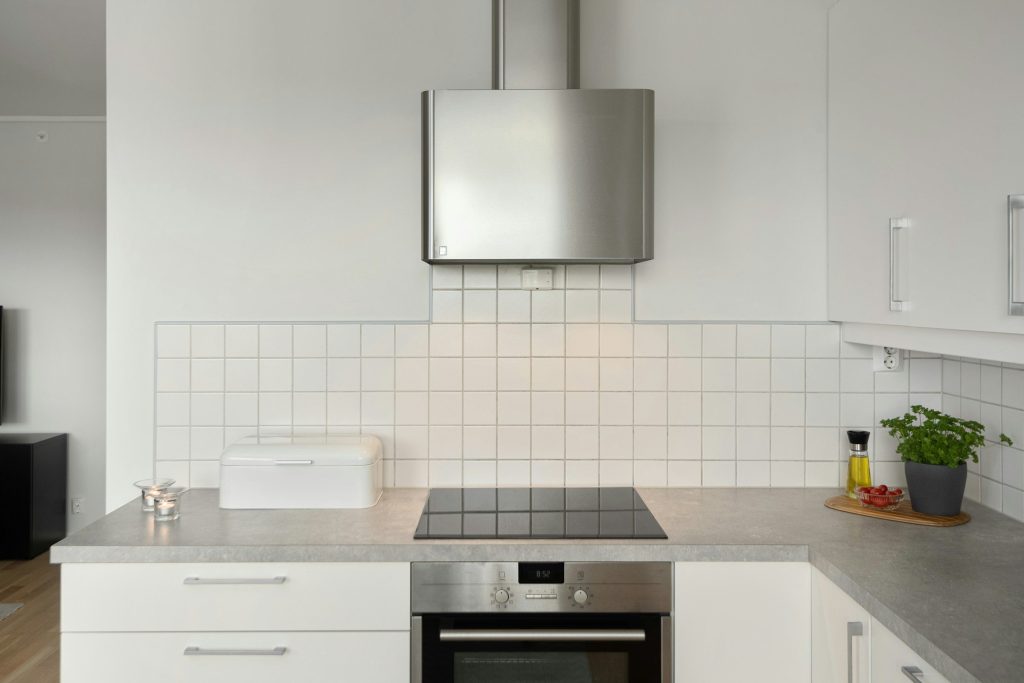 A black glass induction cooktop set into a grey worktop, with a built-in oven below and white tile behind