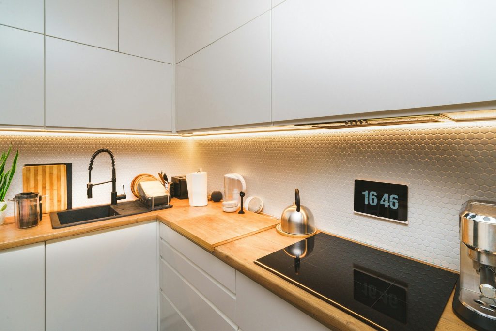 A black induction cooktop set into a long oak worktop in a white kitchen, lit by a warm strip light