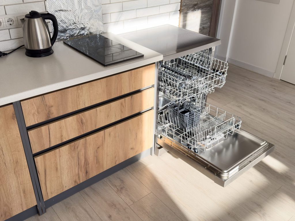 An integrated dishwasher standing open in an oak kitchen, its racks empty and the door lowered