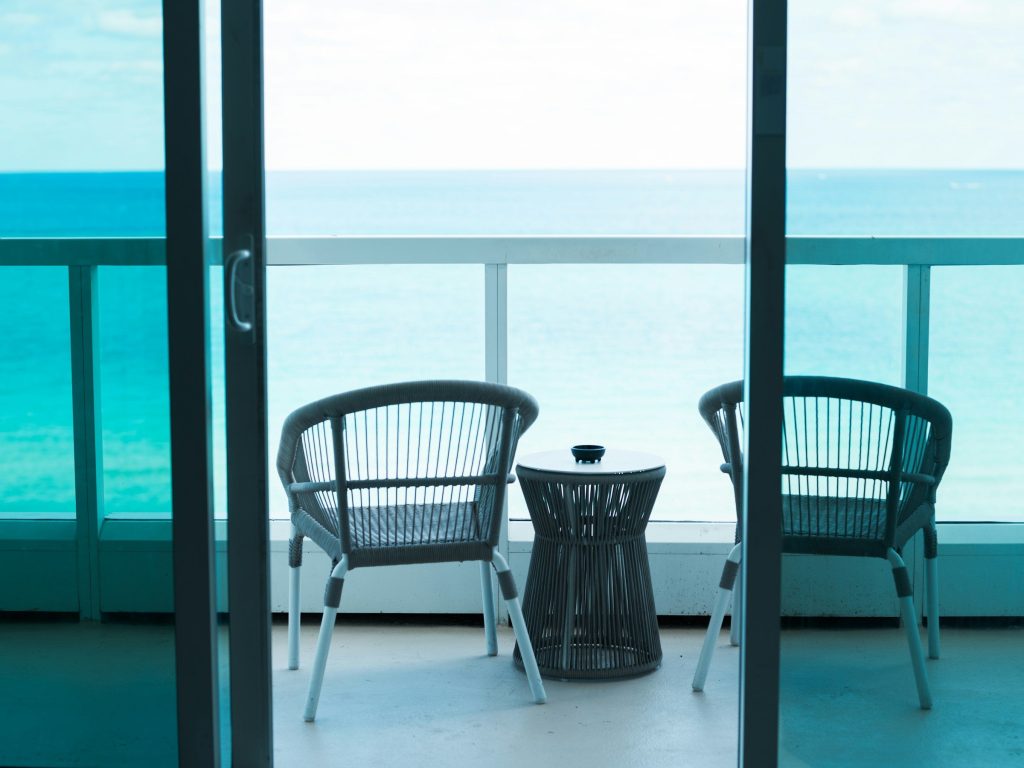 Two chairs on a balcony facing the sea through sliding doors