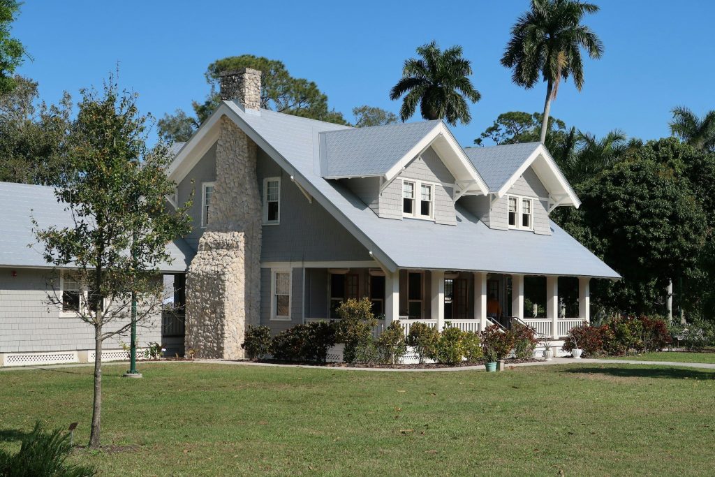A grey shingled bungalow with a stone chimney and a deep porch on a wide lawn