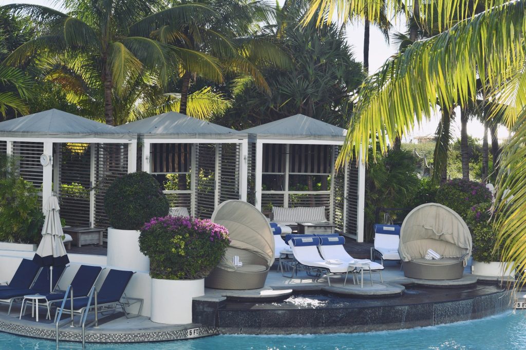 A pool deck with cabanas and daybeds under palms