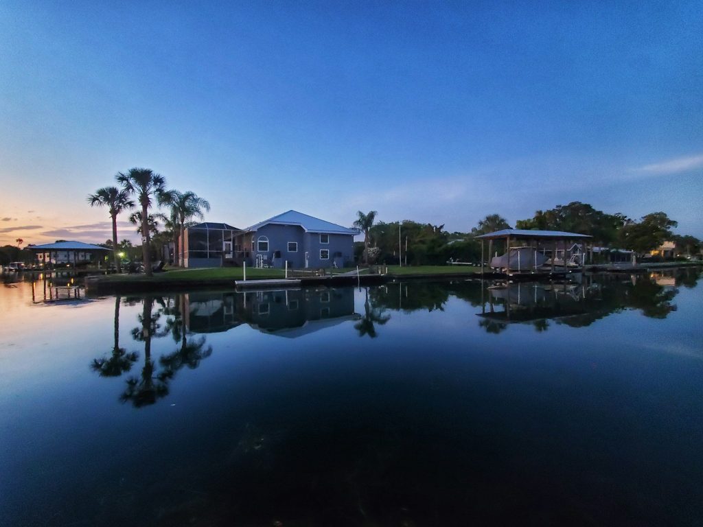 A canal at dusk, houses and palms reflected in flat water