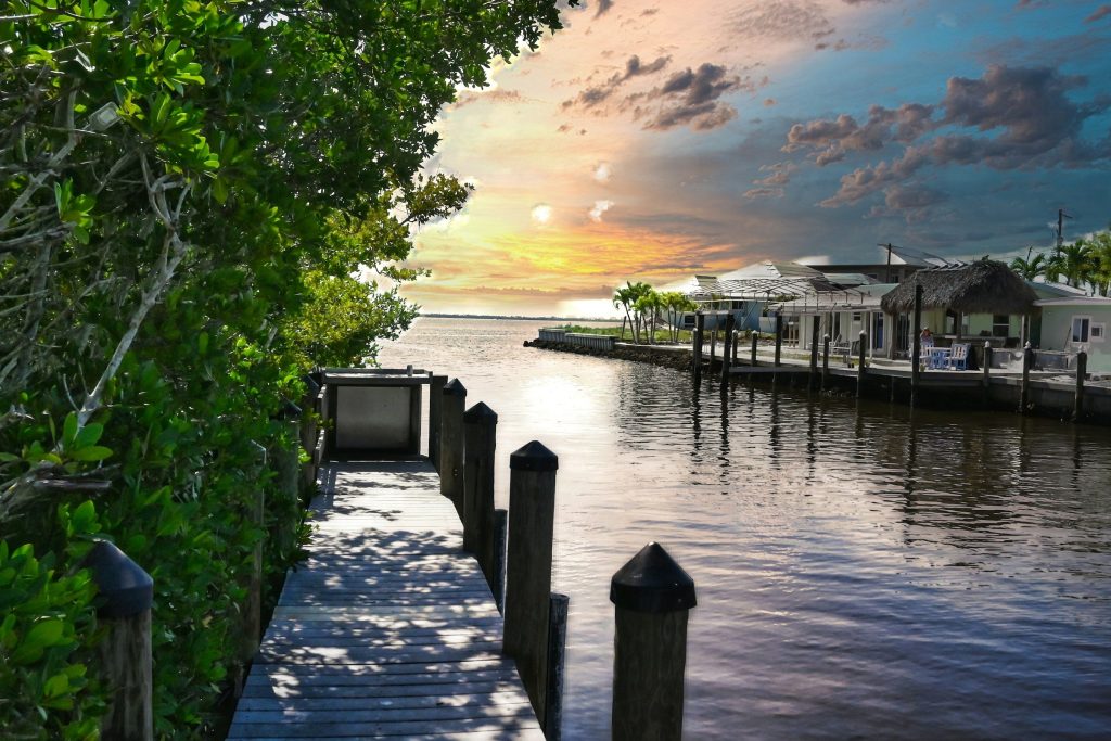 A wooden dock running out to a waterway at sunset, houses along the far bank