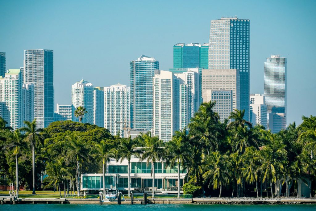 The downtown Miami skyline across the bay, a waterfront house among palms in front of it