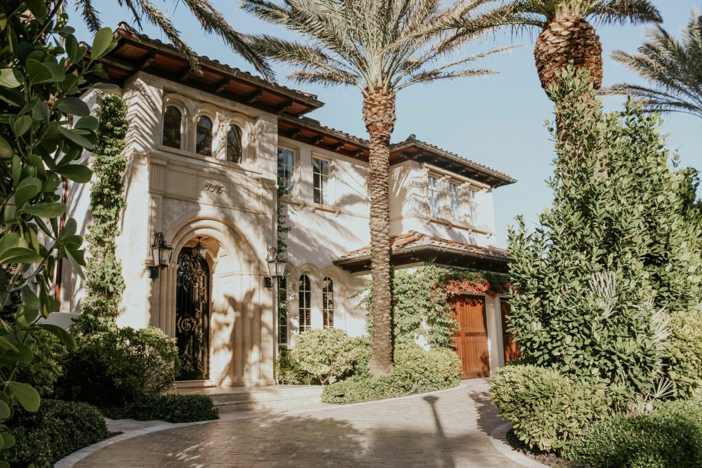 The paver drive and arched entrance of a large Mediterranean house behind date palms