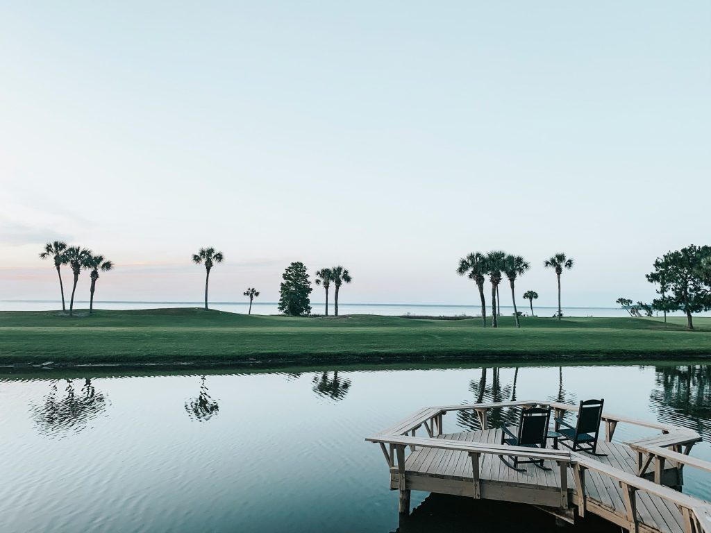 A golf course across a lake at dawn, chairs on a small dock