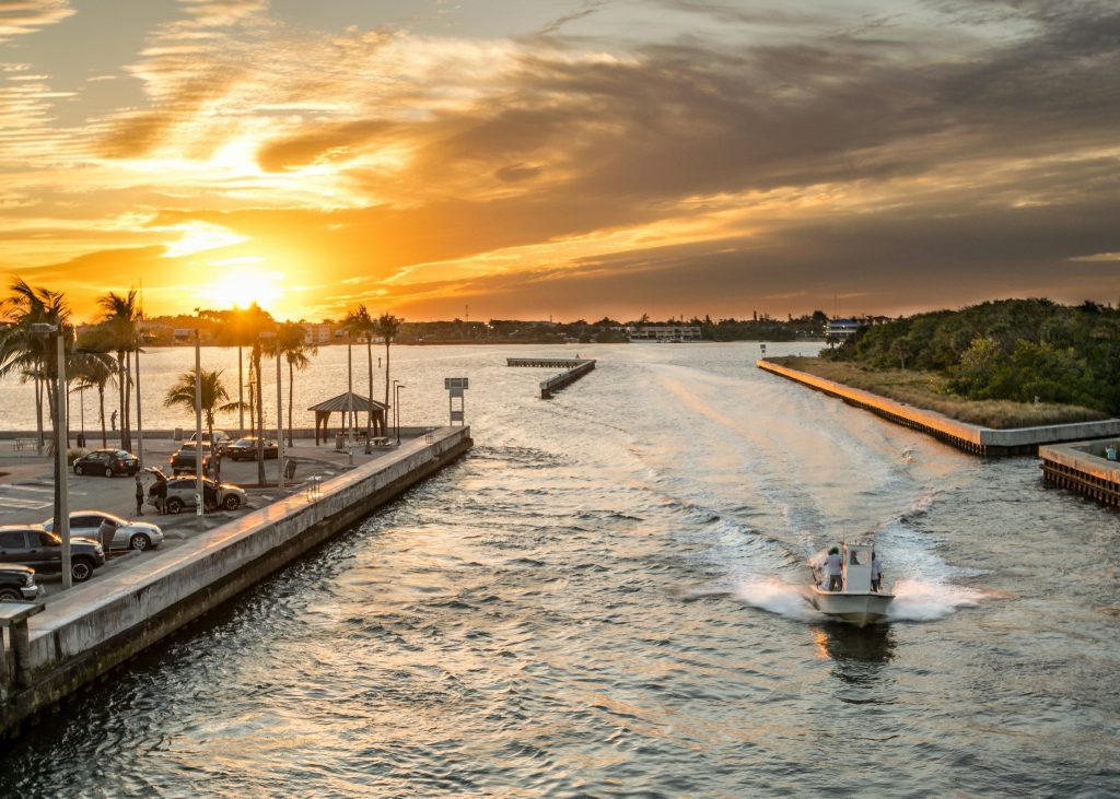 A boat running out through an inlet at sunset past a public dock