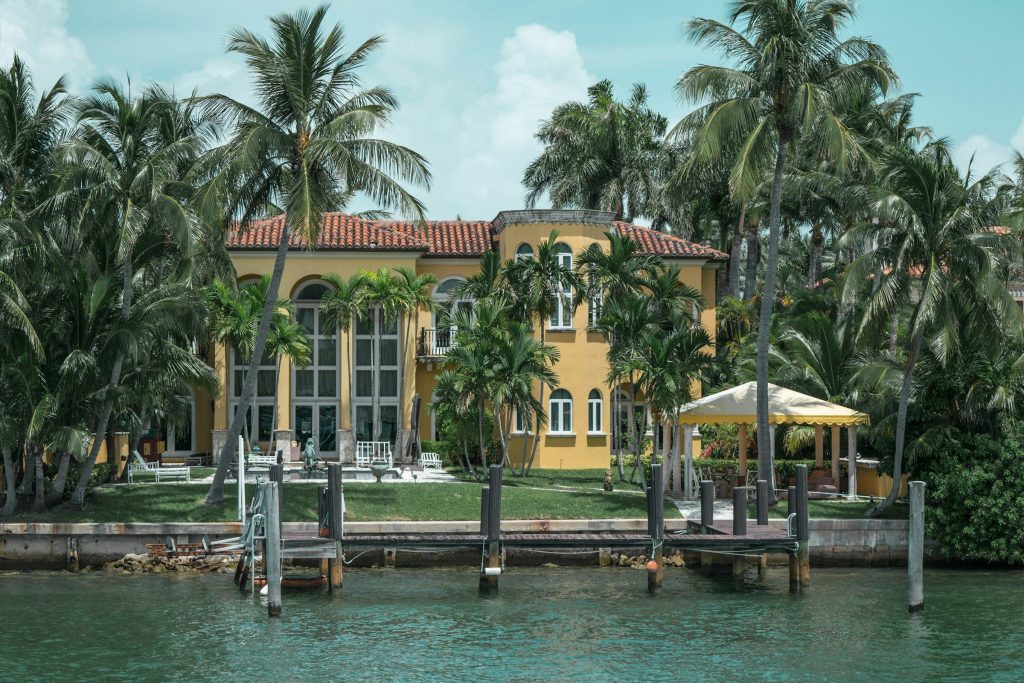 A Mediterranean-style waterfront villa behind coconut palms and a dock
