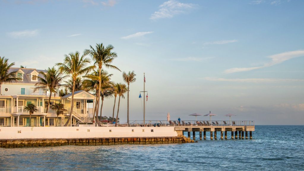 Pale waterfront cottages and a long pier under royal palms