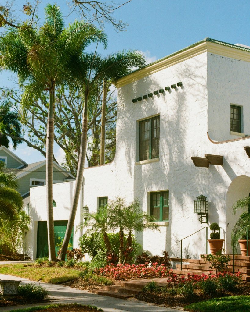 A 1920s white stucco house with a tiled roof, royal palms in the front garden
