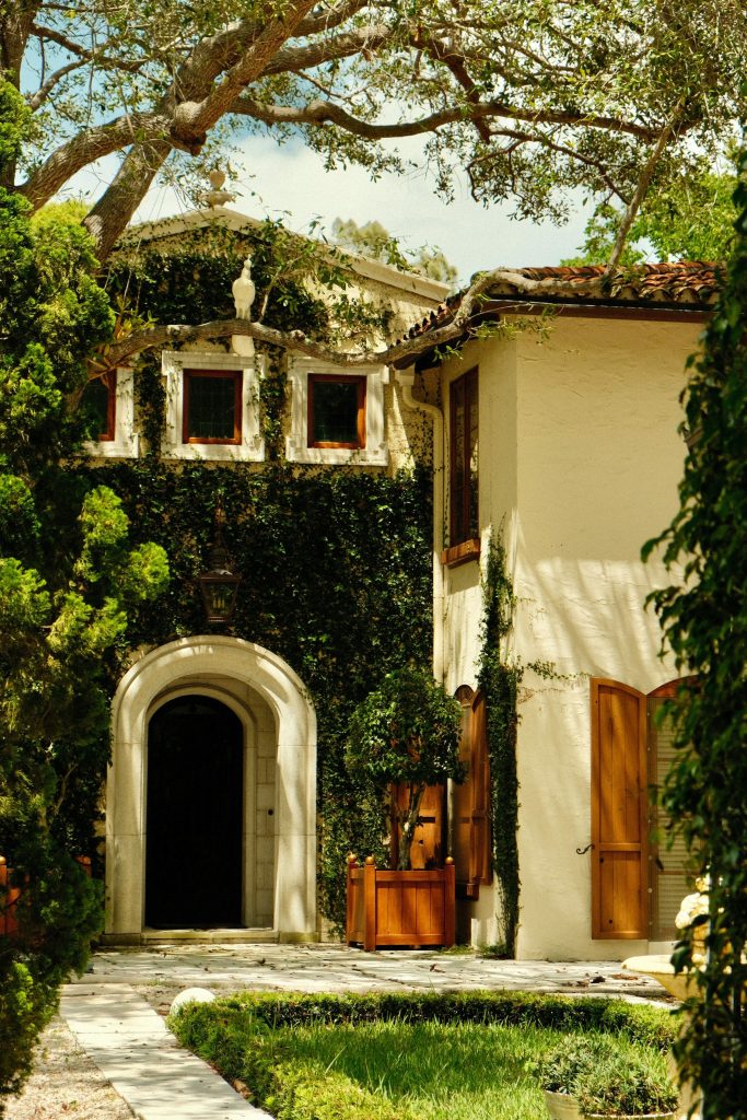 The arched entrance of an ivy-covered Mediterranean revival house under an old oak