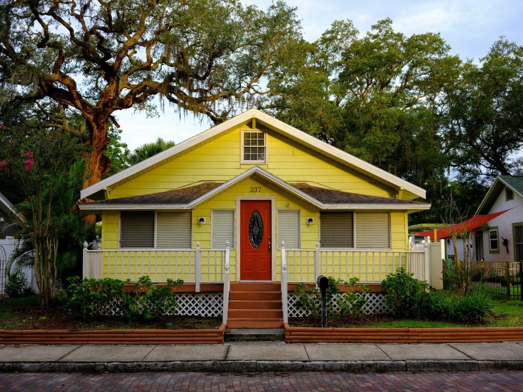 A yellow bungalow with a red door under a live oak hung with Spanish moss