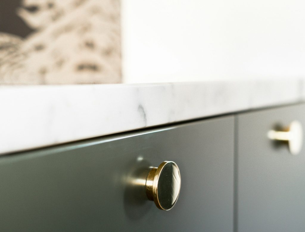 A brass knob on a sage green cabinet door under a marble edge