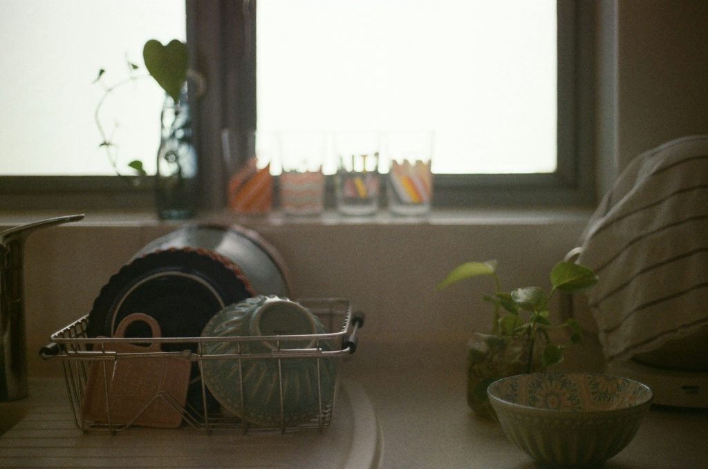 Plates and glasses draining in a rack beside a bright kitchen window