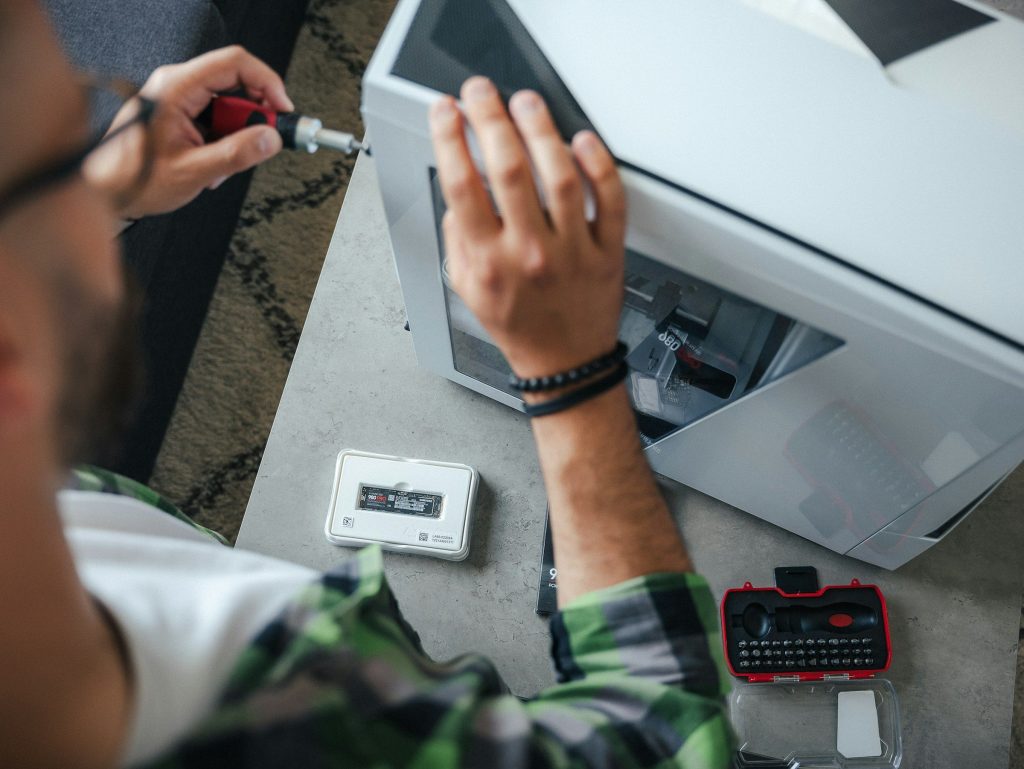 Two hands and a screwdriver at the open panel of a white appliance