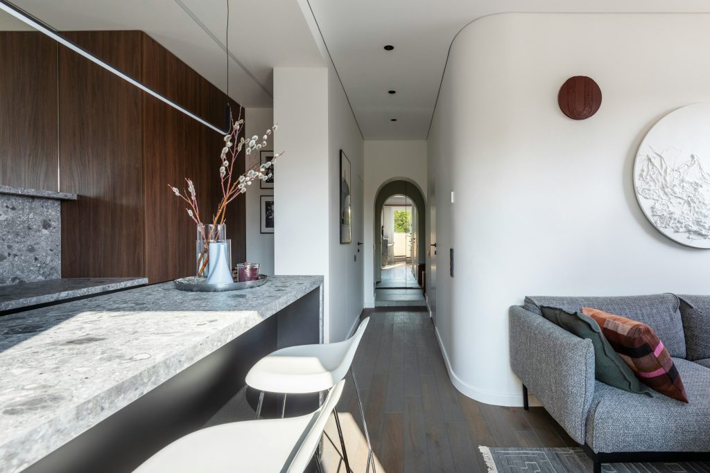 A long stone counter running from a walnut kitchen into a sitting room