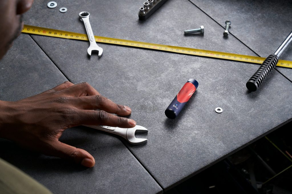 A hand, a spanner, a tape measure and loose fixings on a dark worktop