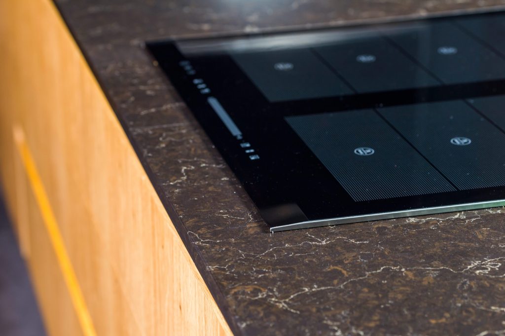 A black glass cooktop set flush into a dark marble counter, seen at a low angle along the glass