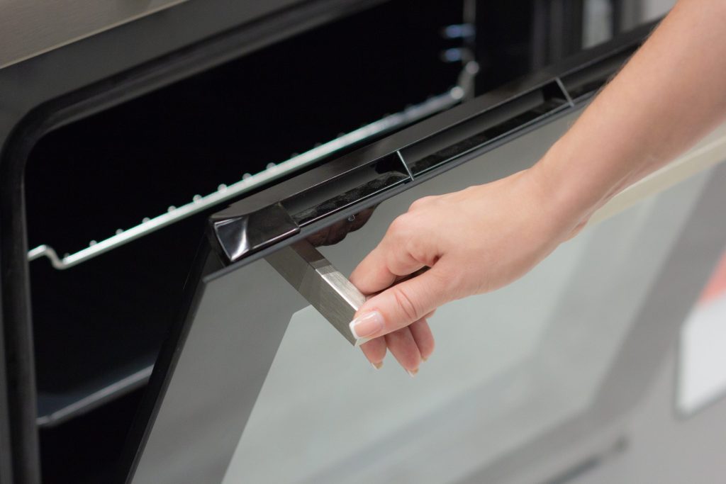 A hand on the steel handle of a black oven door, opening it