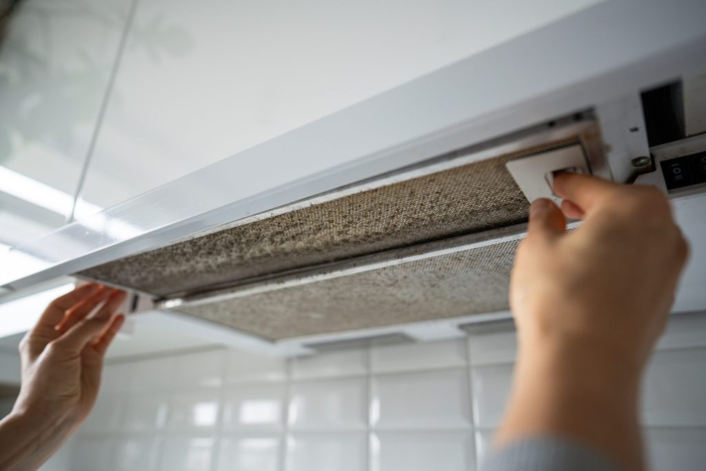 Hands lifting the metal grease filter out of a kitchen extractor hood