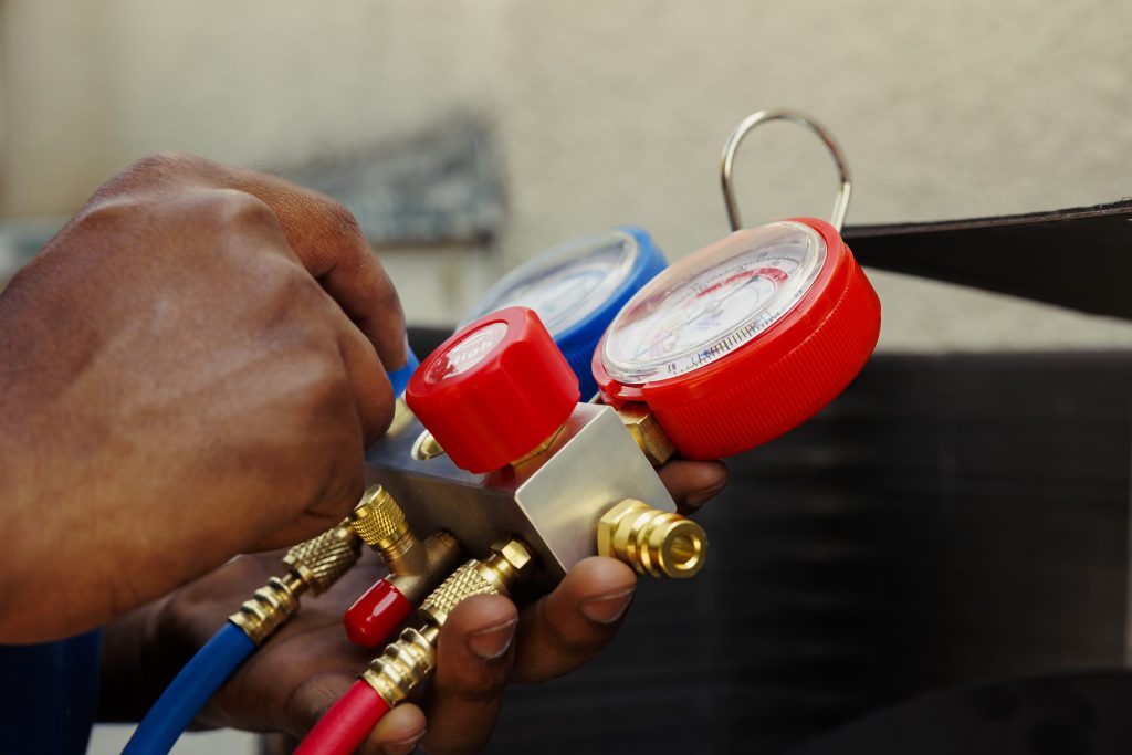 A manifold gauge set held in both hands, the red and blue gauges and hoses in close up