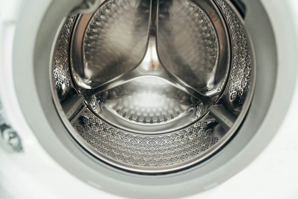 The clean empty stainless drum of a washing machine seen through the open door, paddles and perforations in close up
