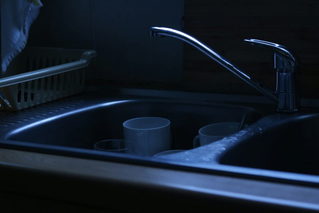 Standing water and two cups in a dark stainless sink