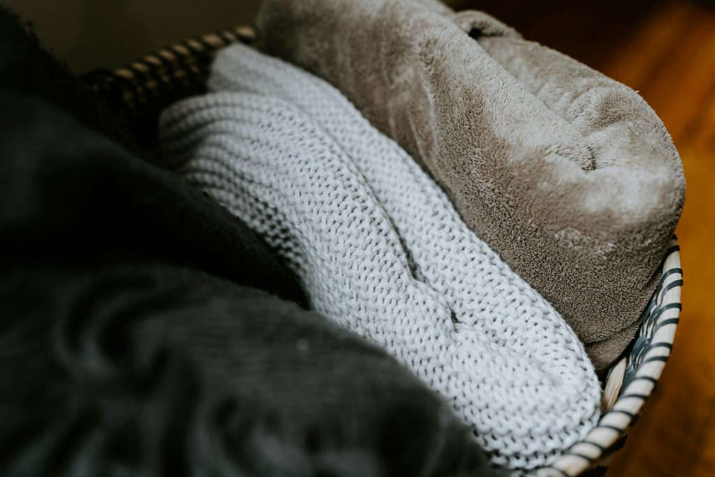 Knitted blankets and a towel folded into a woven basket