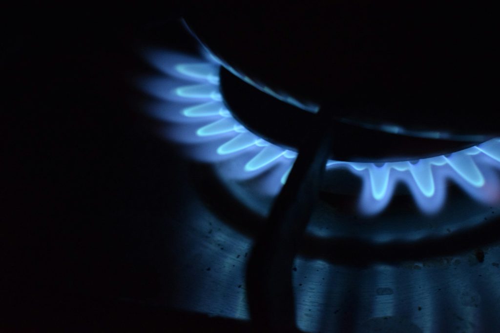 The blue crown of a gas burner alight in a dark kitchen