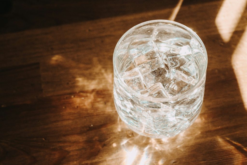 A tumbler of ice on a wooden table in low sun