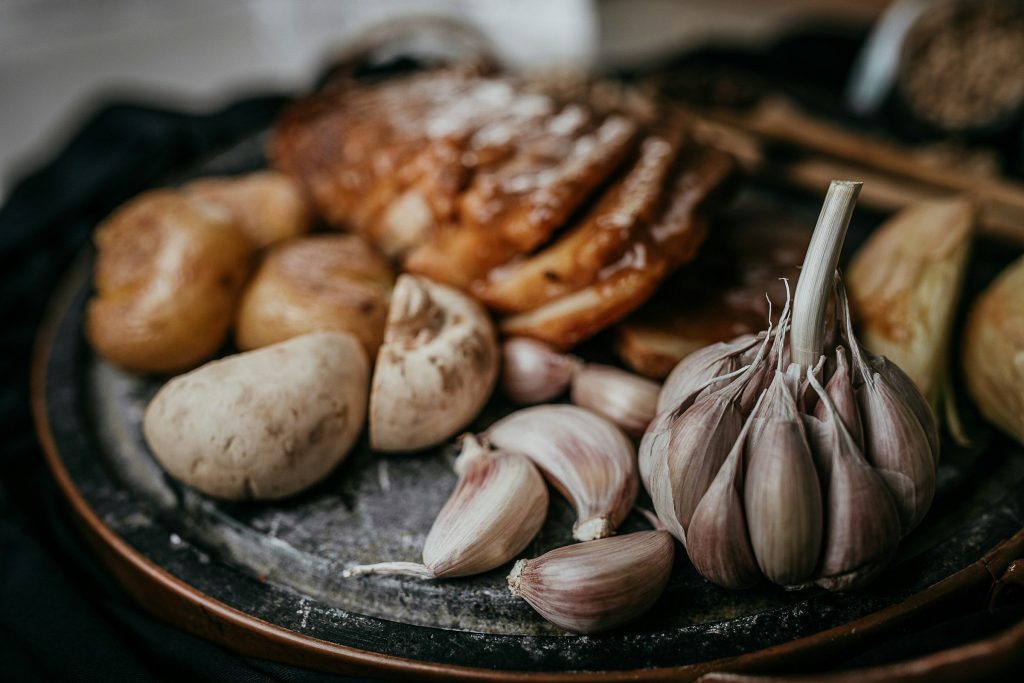 A roast joint with potatoes and garlic waiting on a dark platter