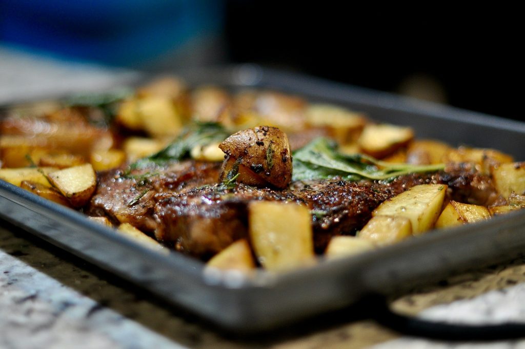 A roasting tray of potatoes and meat, browned unevenly across the pan