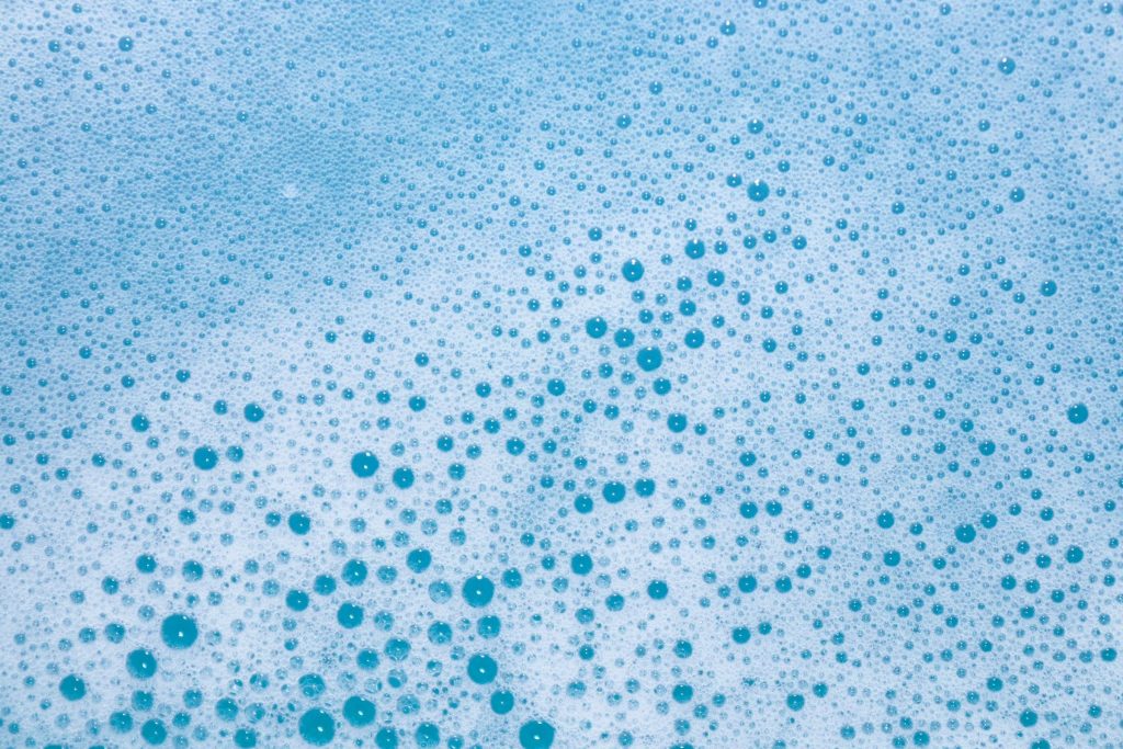 Detergent foam and bubbles across pale blue water