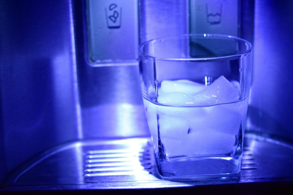A glass being filled with ice under a refrigerator dispenser